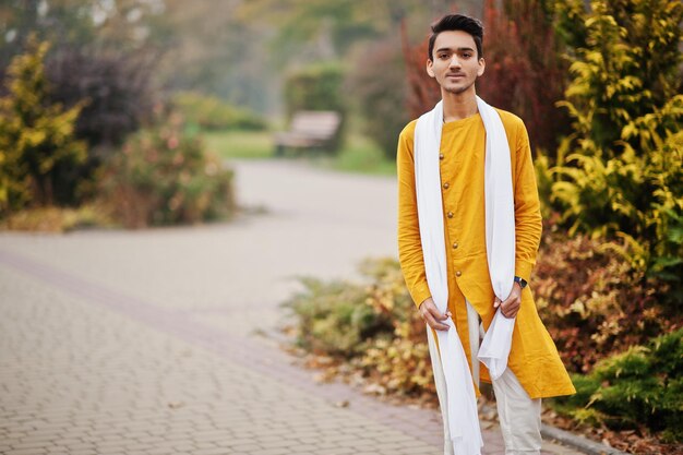 Uomo indiano alla moda in abiti tradizionali gialli con sciarpa bianca in posa all'aperto