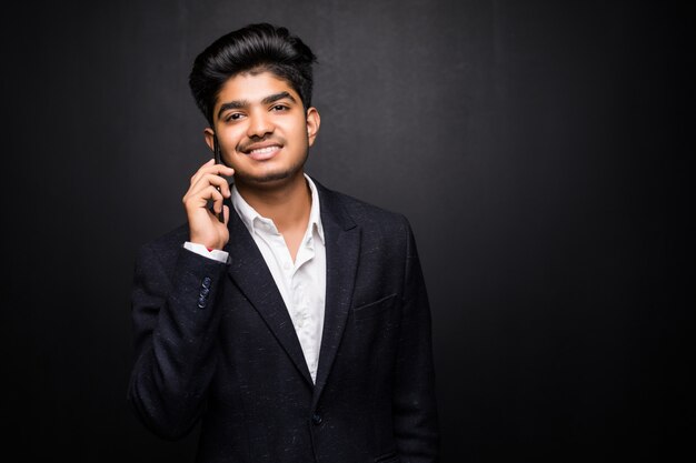 Uomo indiano di affari che parla sul telefono sulla parete nera