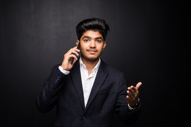 Uomo indiano di affari che parla sul telefono sulla parete nera