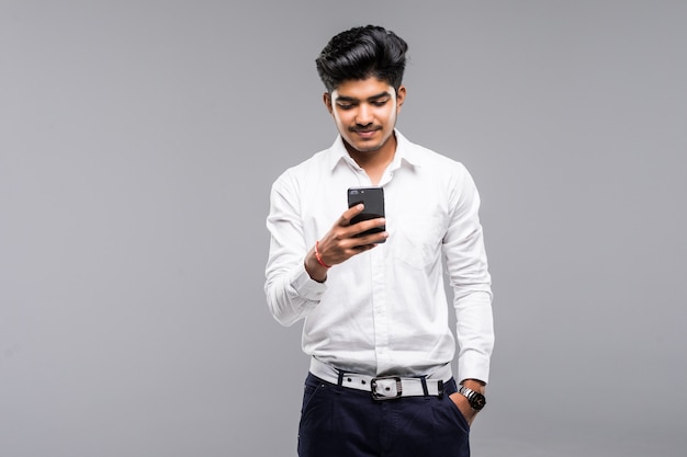 Uomo indiano di affari che per mezzo dello smartphone con la parete bianca