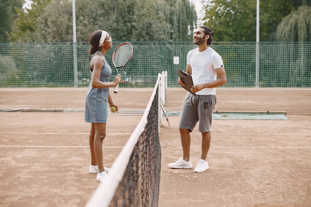 Uomo indiano e donna nera americana in piedi su un campo da tennis