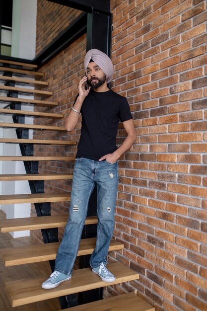 Uomo indiano in turbante beige in piedi sulle scale e parlando al telefono