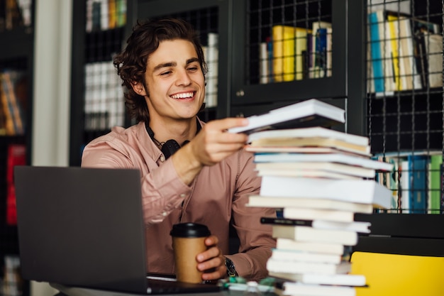 Uomo intellettuale che legge un libro seduto in biblioteca davanti a scaffali con una tazza di caffè sulle mani