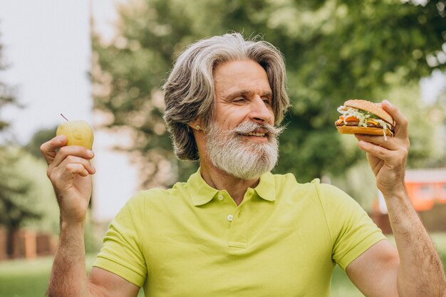 Uomo invecchiato che sceglie tra hamburger e mela