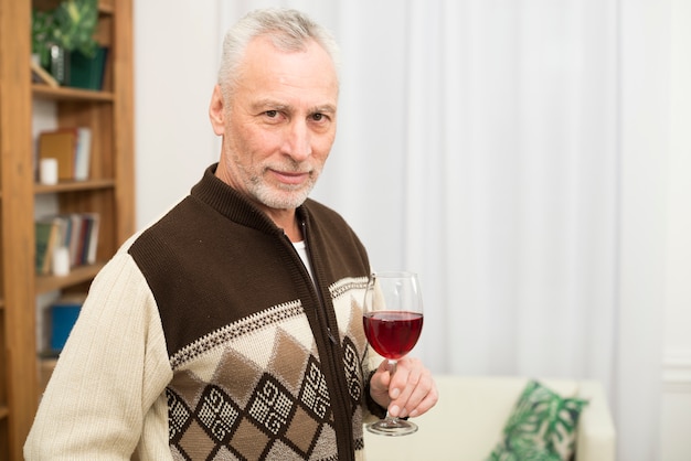 Uomo invecchiato con bicchiere di vino in camera