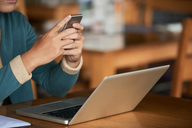 Uomo irriconoscibile che si siede in caffè con il computer portatile e che per mezzo dello smartphone