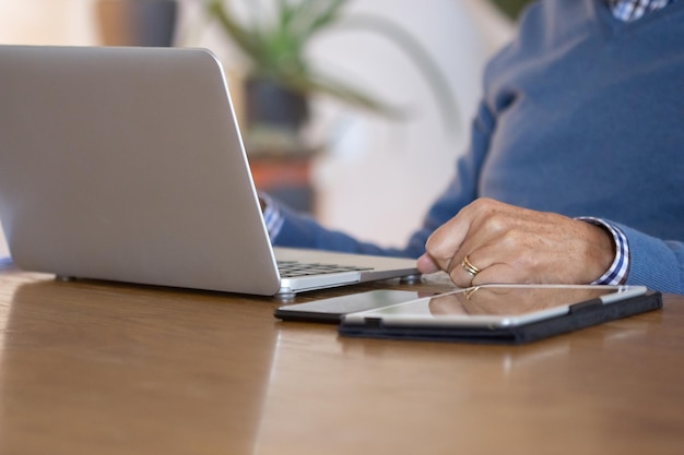 Uomo irriconoscibile che usa il laptop mentre lavora da casa. Primo piano di un uomo d'affari maturo che guarda lo schermo del laptop, seduto al tavolo con tablet e telefono su di esso. Dispositivo digitale, concetto di posto di lavoro