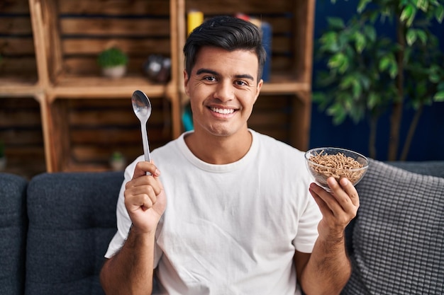 Uomo ispanico che mangia cereali integrali sani con cucchiaio sorridente con un sorriso felice e fresco sul viso che mostra i denti