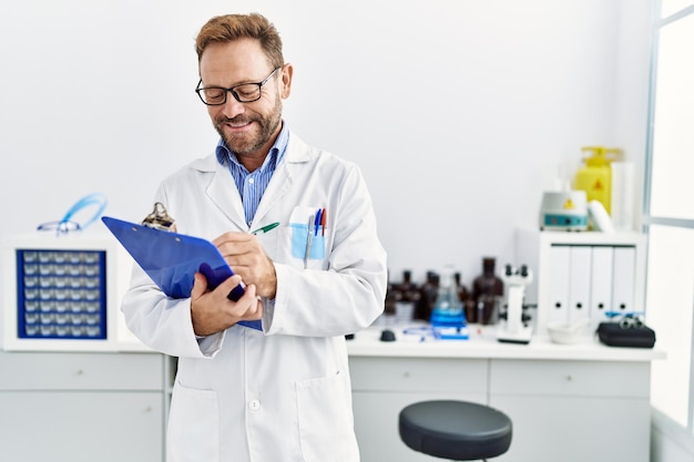 Uomo ispanico di mezza età che sorride fiducioso indossando l'uniforme da scienziato al laboratorio