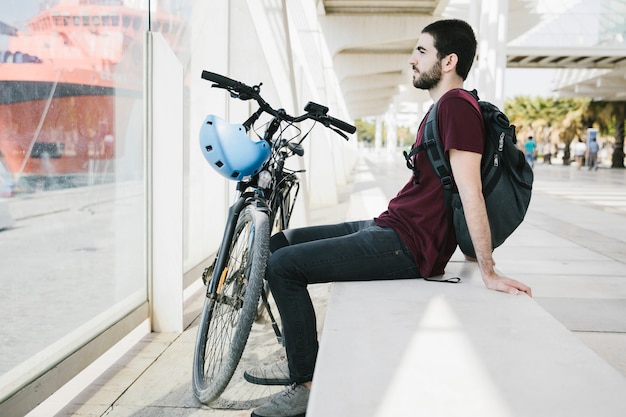 Uomo lateralmente seduto accanto alla bicicletta
