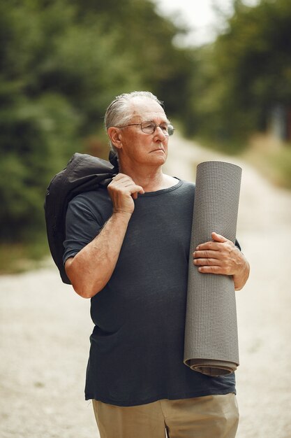 Uomo maggiore al parco estivo. Nonno con una stuoia.