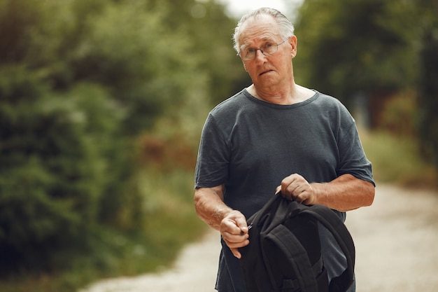 Uomo maggiore al parco estivo. Nonno con uno zaino.