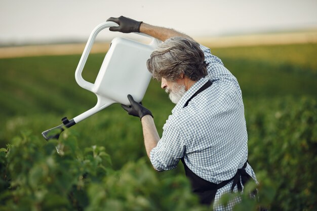 Uomo maggiore che innaffia le sue piante nel suo giardino con cospargere. Uomo con un grembiule nero.