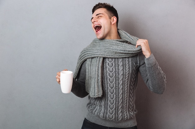 Uomo malato felice in maglione che tiene il suo scraf e la tazza di tè