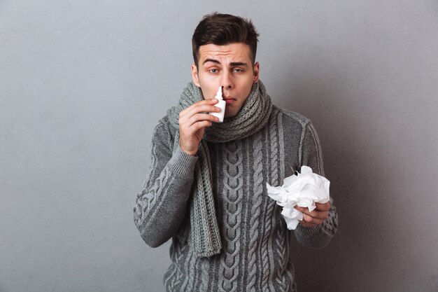 Uomo malato in maglione e sciarpa tenendo il tovagliolo e usando spray mentre guarda