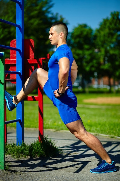 Uomo maschio dell'atleta felice sano sano bello che si esercita al parco della città - concetti di forma fisica un bello giorno di estate sulla barra orizzontale