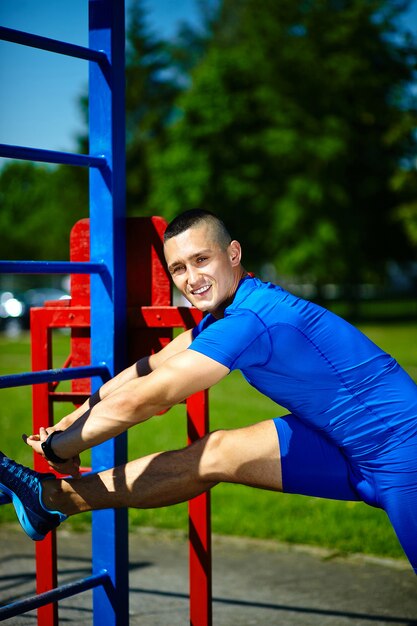 Uomo maschio dell'atleta felice sano sano bello che si esercita al parco della città - concetti di forma fisica un bello giorno di estate sulla barra orizzontale