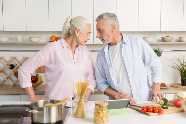 Uomo maturo arrabbiato che sta vicino alla donna seria matura alla cucina