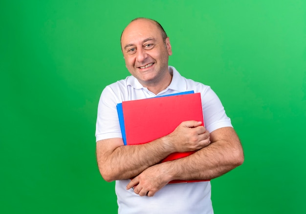 Uomo maturo casuale sorridente che tiene le cartelle isolate sulla parete verde