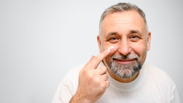 Uomo maturo che mette la crema per la cura della pelle sul suo fronte