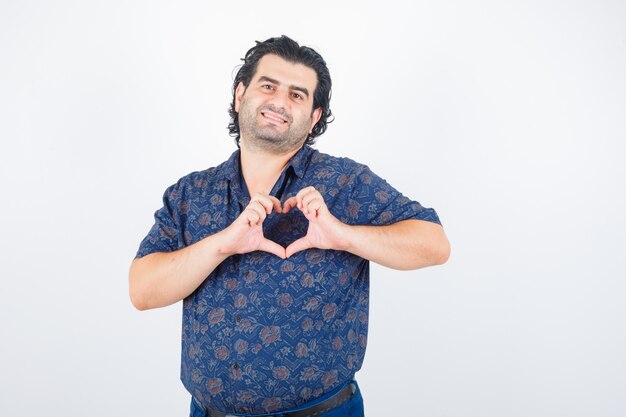 Uomo maturo che mostra il gesto del cuore in camicia e che sembra felice. vista frontale.