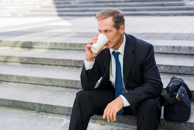 Uomo maturo che si siede sulla scalinata bevendo caffè