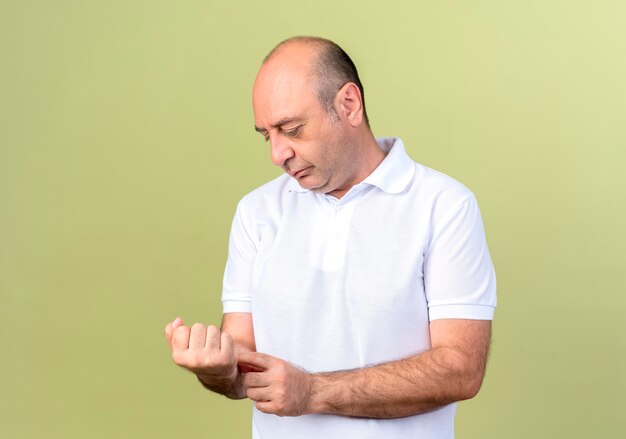 Uomo maturo di pensiero che osserva e che mette a disposizione sul polso isolato sulla parete verde oliva