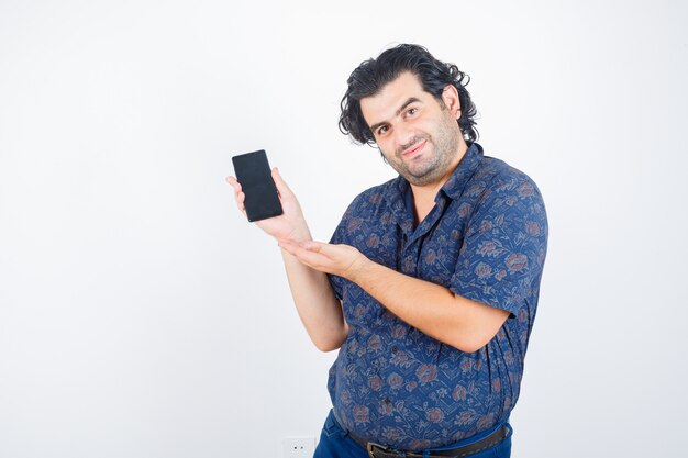 Uomo maturo in camicia che presenta il telefono cellulare e che sembra fiducioso, vista frontale.