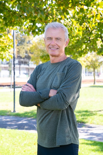 Uomo maturo positivo con braccia incrociate in piedi fuori, ae sorridente. Colpo verticale. Persona sportiva matura o concetto di stile di vita attivo