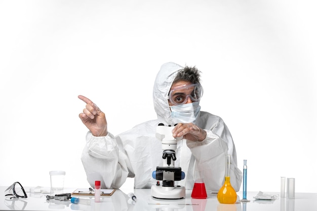 uomo medico in tuta protettiva e maschera usando il suo microscopio su bianco