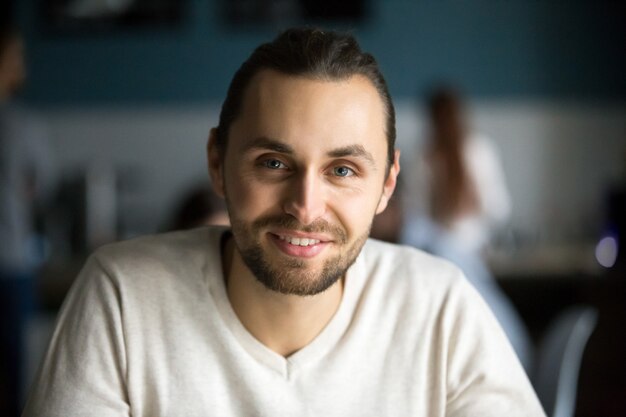 Uomo millenario sorridente che esamina macchina fotografica in caffè, ritratto di colpo in testa