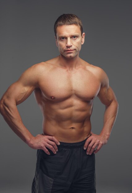 Uomo muscolare senza camicia di mezza età isolato su uno sfondo grigio.
