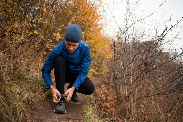 Uomo nella foresta che si allaccia i lacci delle scarpe