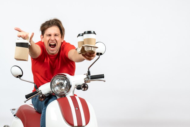 Uomo nervoso del corriere emotivo in uniforme rossa che si siede sulla moto che consegna gli ordini su priorità bassa bianca