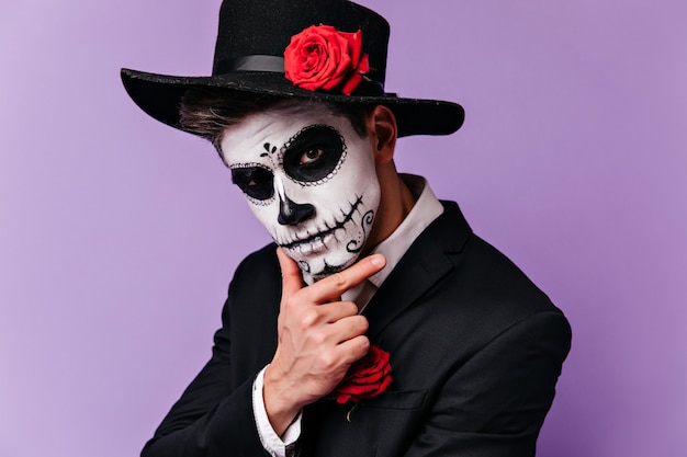 Uomo pensieroso con il trucco messicano tradizionale che osserva alla macchina fotografica. Studio shot del ragazzo in abito da zombie in posa prima della festa di halloween.