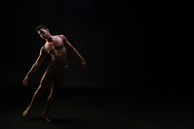 Uomo piegato atletico nudo che sta sul fondo nero