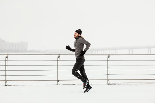 Uomo pieno del colpo che corre con la neve