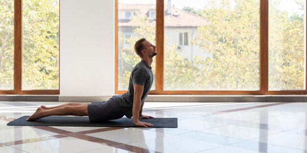 Uomo pieno del colpo che fa il cane rivolto verso l'alto sul materassino yoga all'interno