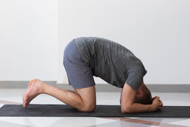 Uomo pieno del colpo che fa posa di yoga dell'interno