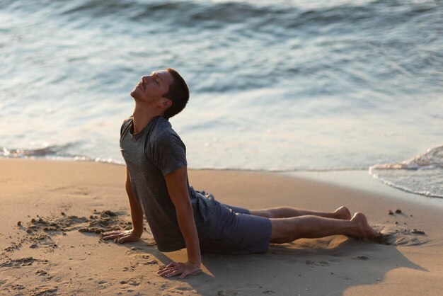 Uomo pieno del colpo che fa posa di yoga sulla spiaggia