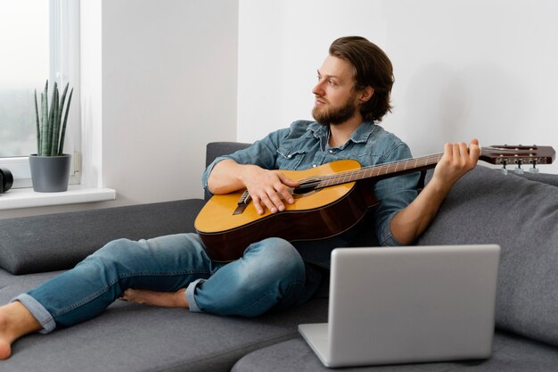 Uomo pieno del colpo che gioca chitarra a casa