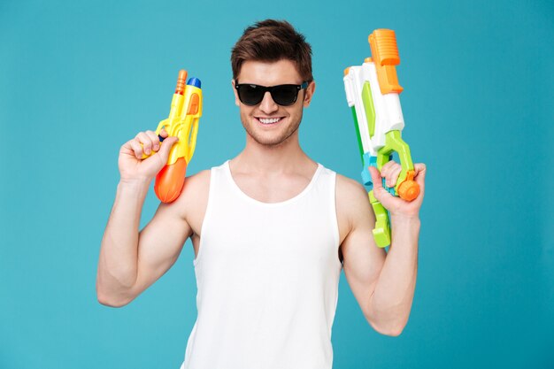 Uomo positivo che guarda macchina fotografica e che tiene due pistole a acqua