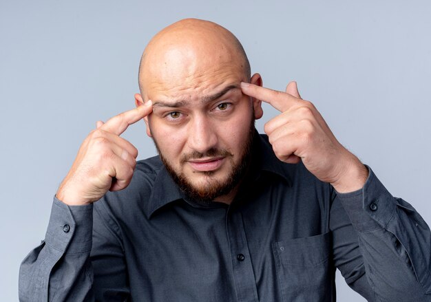 Uomo premuroso giovane call center calvo che mette le dita sulle tempie guardando la parte anteriore isolata sul muro bianco