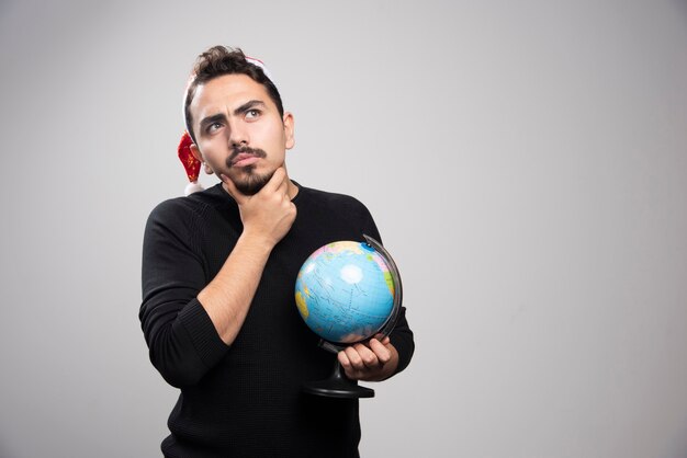 Uomo premuroso in cappello di Babbo Natale in posa con il globo.