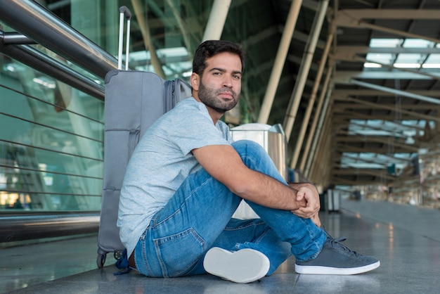 Uomo premuroso stanco che si siede sul pavimento all'aeroporto