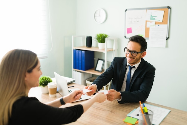 Uomo professionale felice che sorride e scambia biglietti da visita con una collega. Donna caucasica che dà il suo numero e le informazioni di contatto a un uomo latino in giacca e cravatta