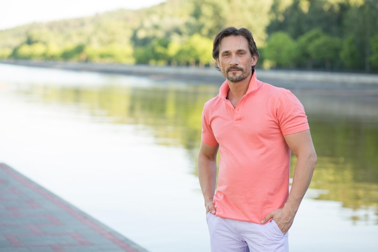Foto gratuito uomo ricco che posa per il fotografo con le braccia in tasca isolate sul fiume. uomo di mezza età con una maglietta di corallo a causa di un'enorme fabbrica.