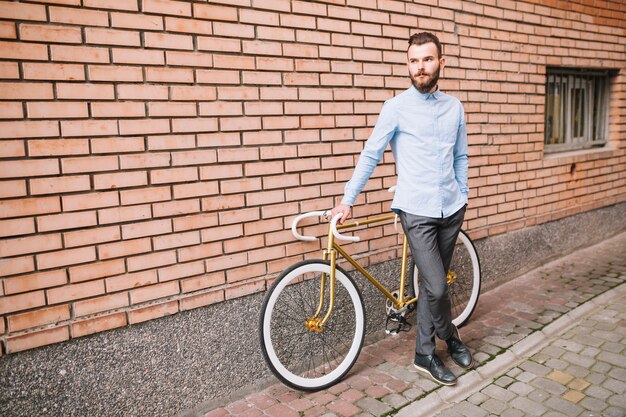 Uomo rilassato con la bicicletta vicino al muro di mattoni