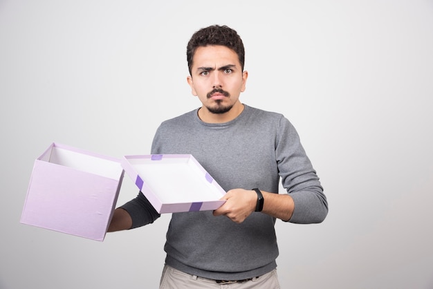 Uomo scioccante che apre una scatola viola su un muro bianco.