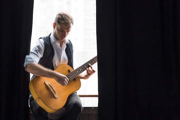 Uomo seduto alle finestre a suonare la chitarra